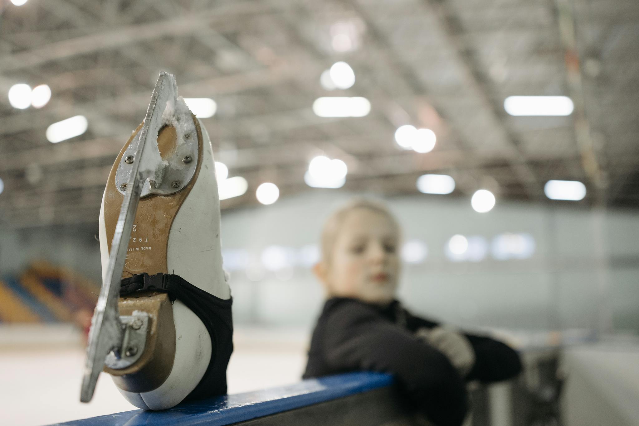 A child resting with a raised ice skate in an indoor rink. Capturing the spirit of figure skating.