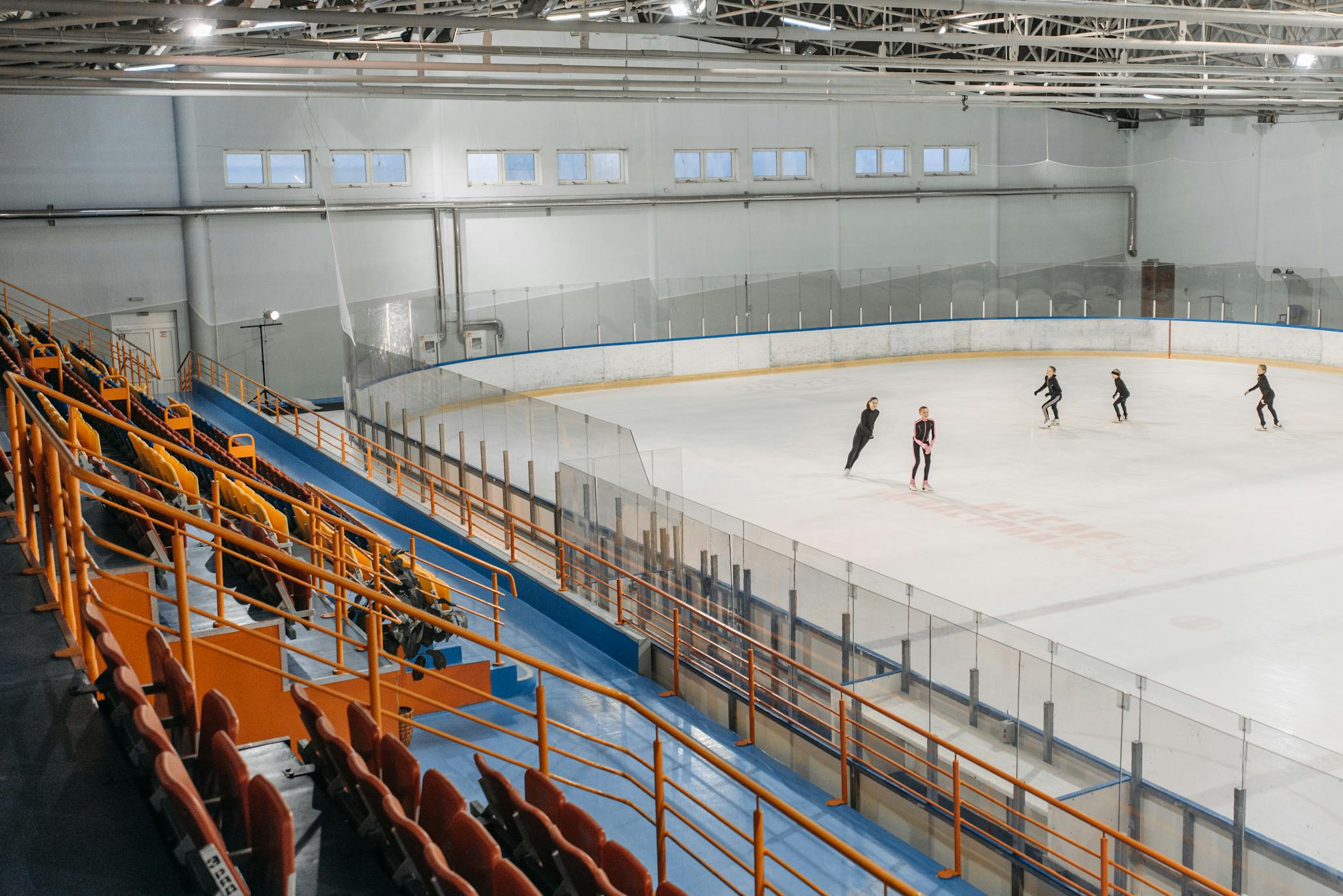 A group of skaters practicing on an indoor ice rink in a stadium setting.