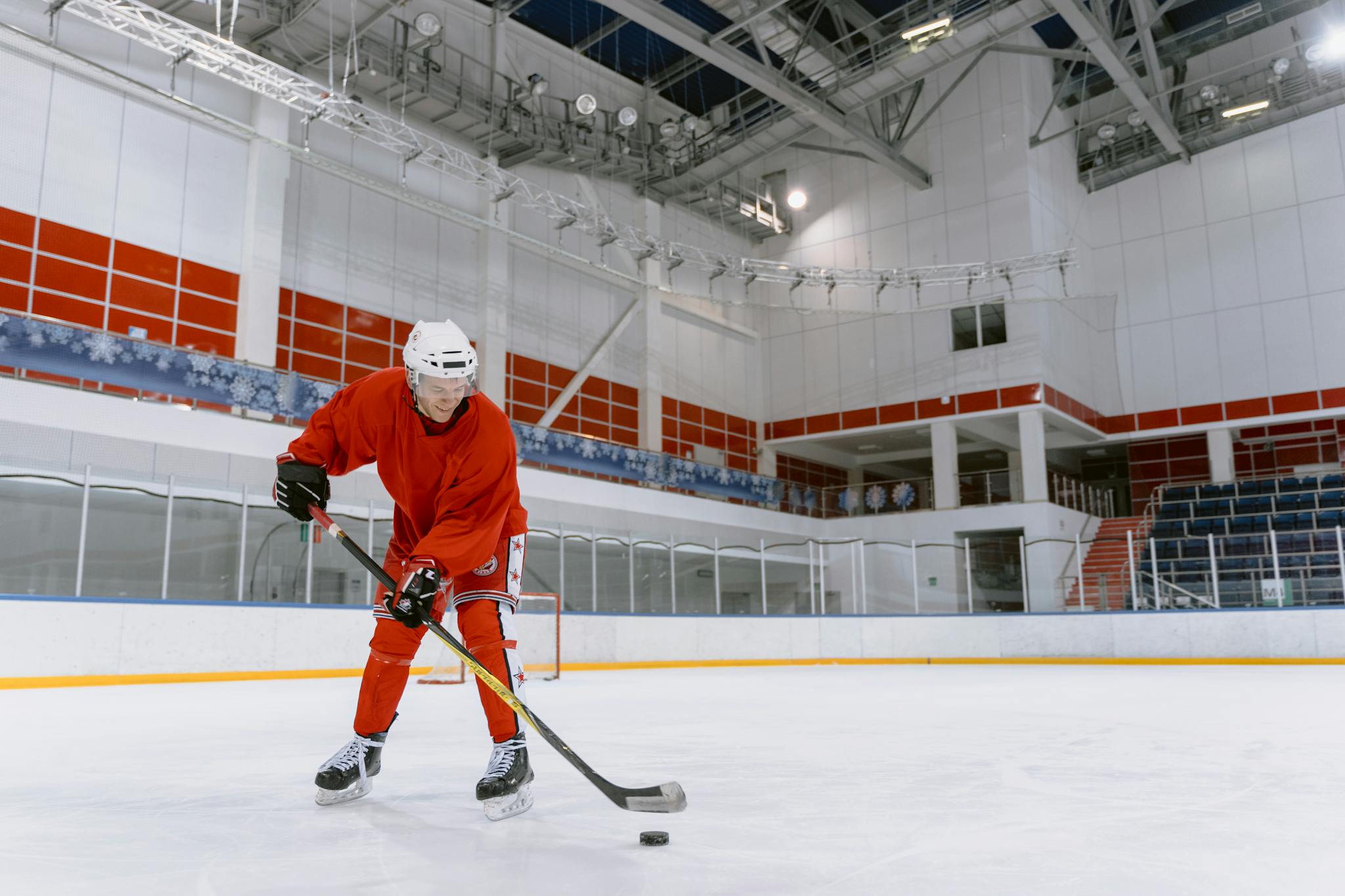 Focused ice hockey player in red gear practicing on an indoor rink, showcasing skill and movement.