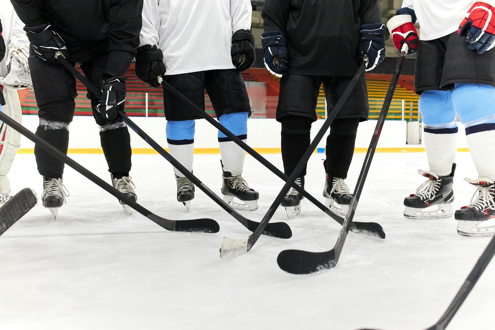 Hockey players in gear forming a circle on ice, holding sticks.